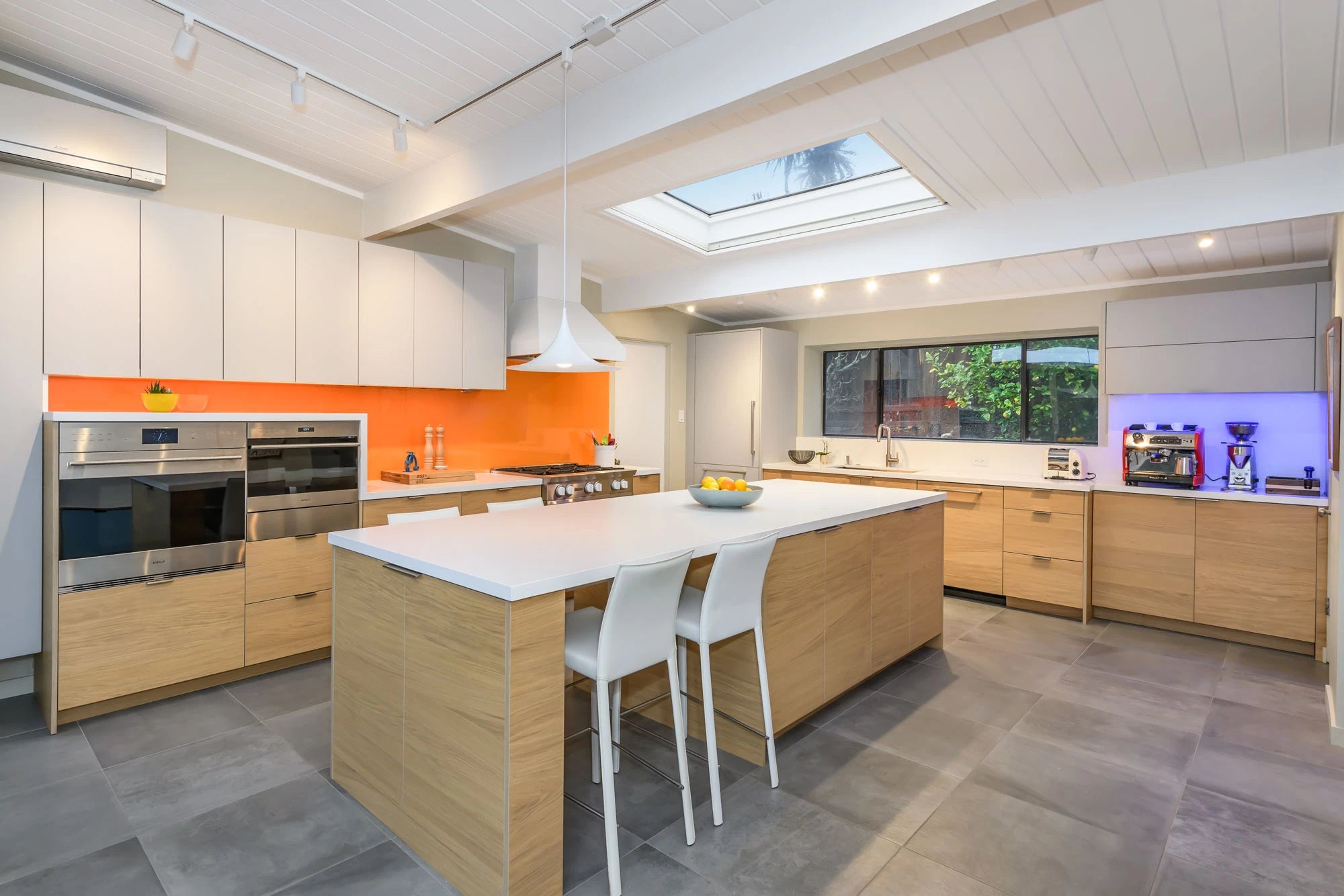 Natural wood and white kitchen cabinetry with an orange backsplash and skylight