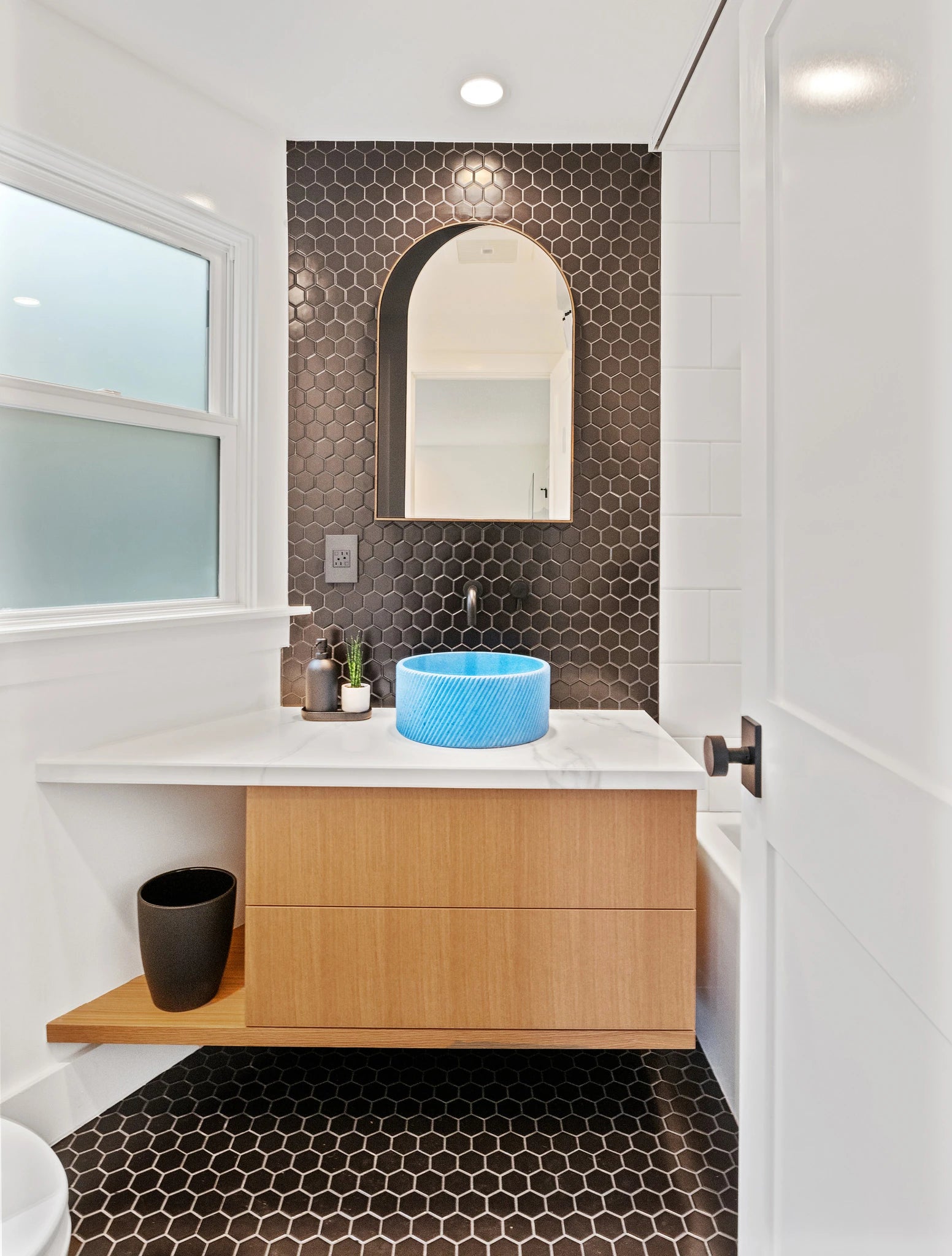 Floating wood vanity with a blue vessel sink and geometric tile in a compact bathroom